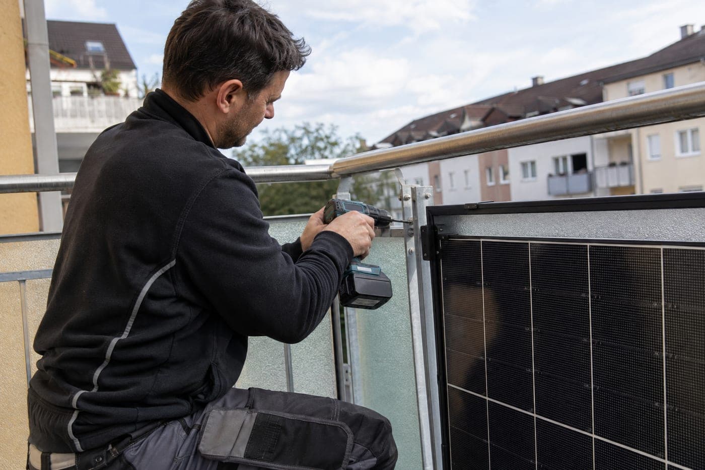 Monteur befestigt ein Solarmodul mit dem Akkuschrauber am Balkongeländer