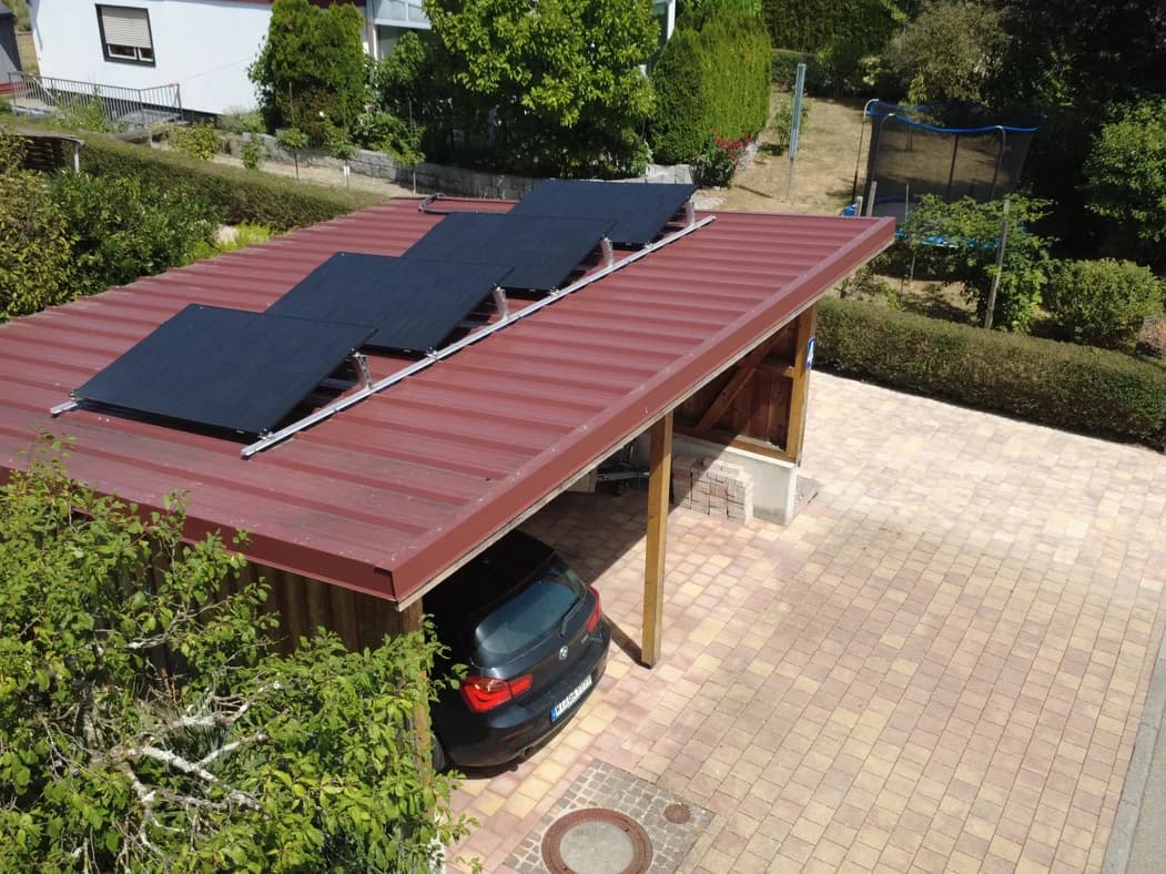 Vier Solarmodule auf einem roten Blechdach über einem Carport